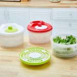 Essoreuses à salade manuelles en plastique blanc, rouge et vert sur un plan de travail de cuisine.