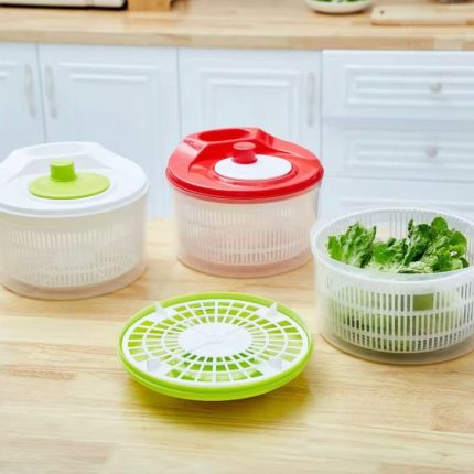 Essoreuses à salade manuelles en plastique blanc, rouge et vert sur un plan de travail de cuisine.