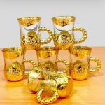 Ensemble de six tasses en verre transparent avec socle et poignées perlées en métal doré finement ciselé.