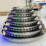 Pile de sept plateaux de service ronds en acier inoxydable avec bordures à motifs diamantés.