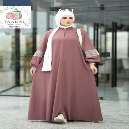Robe abaya évasée de couleur vieux rose avec de magnifiques détails brodés sur les manches bouffantes, portée avec un hijab blanc.