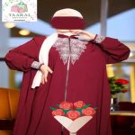 Femme portant une abaya bordeaux fluide avec fermeture éclair sur le devant et de riches broderies blanches au col et aux poignets.