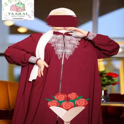 Femme portant une abaya bordeaux fluide avec fermeture éclair sur le devant et de riches broderies blanches au col et aux poignets.