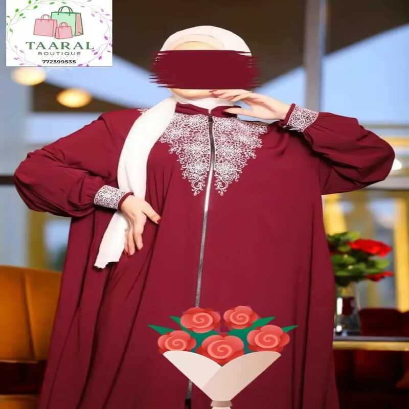 abaya-zip-brodee-bordeaux-taaral Femme portant une abaya bordeaux fluide avec fermeture éclair sur le devant et de riches broderies blanches au col et aux poignets.