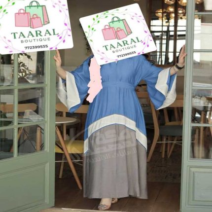 Femme portant une abaya style kimono moderne bicolore et tricolore en pans de tissus bleu jean, blanc crème et gris, resserrée à la taille.