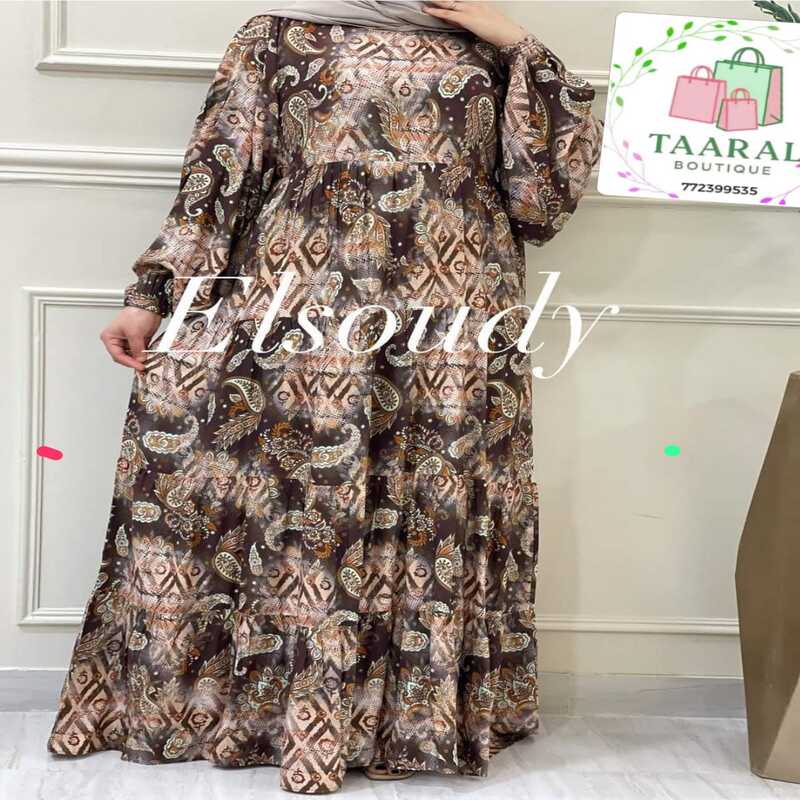 robe-longue-evasee-motifs-imprimes-taaral-boutique Femme portant une robe longue évasée à motifs imprimés de style ornemental et géométrique dans les tons vert, marron et beige, avec des manches longues bouffantes, par Taaral Boutique.