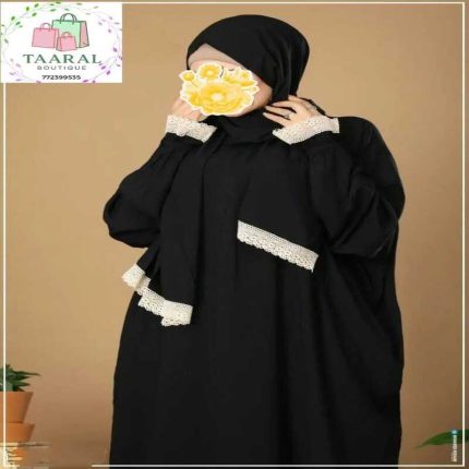 Femme portant un ensemble de mode pudique noir opaque composé d'une abaya ample et d'un voile assorti, tous deux ornés d'une large bordure en dentelle blanche ou crème sur les poignets, les poches et le bas du voile, par Taaral Boutique.