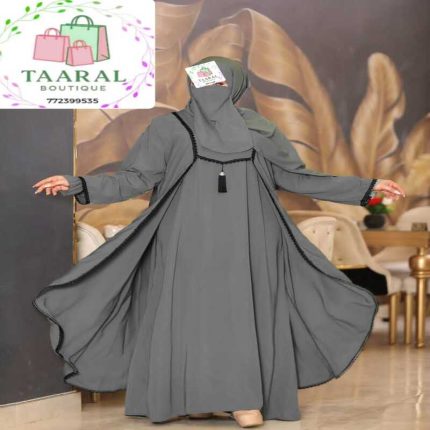 Femme portant un ensemble de mode pudique entièrement noir composé d'une robe intérieure et d'un long manteau ouvert assorti orné de liserés sombres élégants et d'un petit pompon sur le buste, par Taaral Boutique.