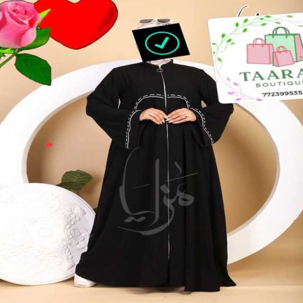Femme portant une abaya longue de couleur noire, dotée d'une fermeture éclair argentée sur toute la longueur à l'avant et de surpiqûres blanches décoratives sur le buste et les manches amples, par Taaral Boutique.