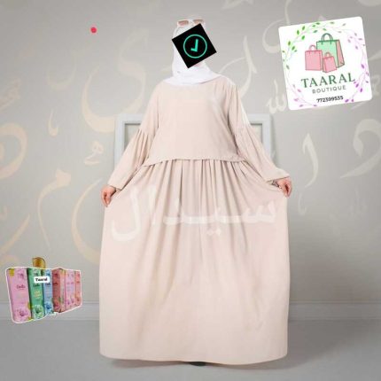 Femme portant un ensemble moderne composé d'une robe longue plissée et d'un manteau court superposé assorti à manches longues.