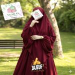 Femme portant un jilbab moderne composé d'une robe longue fluide et d'un khimar à plusieurs niveaux avec niqab intégré, à côté d'un portant de vêtements de Taaral Boutique.