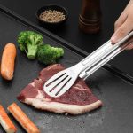 Pince à barbecue en acier inoxydable saisissant une viande sur une plaque de cuisson.
