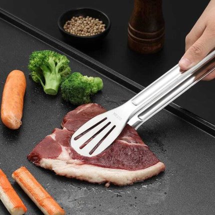 Pince à barbecue en acier inoxydable saisissant une viande sur une plaque de cuisson.
