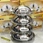 Ensemble de quatre plats de service ronds en acier inoxydable empilés, de tailles 35cm, 40cm, 45cm et 50cm, avec couvercles bombés et poignées dorées.