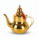 Théière marocaine traditionnelle en acier inoxydable doré brillant avec un pompon rouge suspendu au couvercle, isolée sur fond blanc.