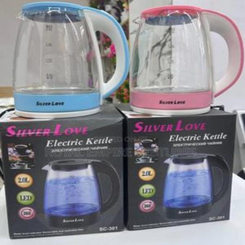Deux bouilloires électriques en verre transparent de marque Silver Love, l'une bleue et l'autre rose, posées sur leurs boîtes d'emballage respectives.