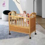 Lit évolutif pour bébé en bois massif sur roulettes, équipé d'un espace de rangement inférieur et d'une petite tablette d'activités avec un enfant debout à l'intérieur.