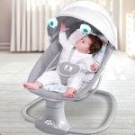 Balancelle électrique pour bébé de la marque Mastela avec un harnais de sécurité à 5 points, une capote de protection et de petites peluches suspendues en forme d'éléphant, montrant un bébé installé à l'intérieur.