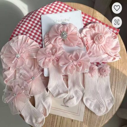 Coffret d'accessoires pour bébé de la marque Chicbaby présenté sur un support en bois, comprenant un bonnet de style turban orné d'un grand nœud strassé et une paire de chaussettes hautes assorties avec des nœuds décoratifs.