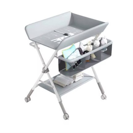 Table à langer pliable pour bébé montée sur des pieds en métal en X avec des roulettes, équipée d'un matelas à langer avec ceinture de sécurité, d'un panier de rangement latéral compartimenté et d'une étagère inférieure en tissu.