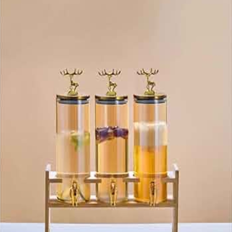distributeur-boisson-triple-support-cerf rois distributeurs de boissons verticaux en verre transparent disposés sur un support, dotés de robinets et de couvercles ornés d'une figurine de cerf dorée.