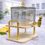 Distributeur de boissons carré en verre transparent avec robinet et couvercle hermétique, posé sur un support surélevé à double étage dans une cuisine lumineuse.