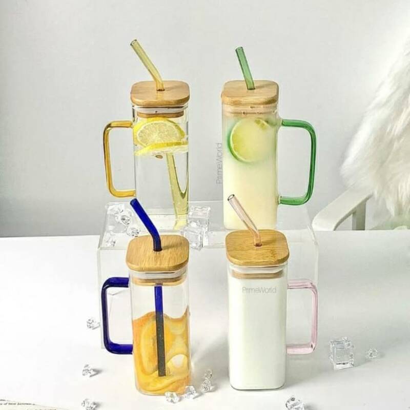 gobelet-verre-carre-couvercle-bambou-paille Quatre gobelets carrés en verre transparent avec anses, surmontés de couvercles en bois et équipés de pailles en verre, contenant différentes boissons avec des tranches d'agrumes et entourés de glaçons.