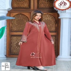 Jeune fille portant une longue abaya ou djellaba égyptienne marron brique avec des ornements de strass dorés devant de grandes portes en bois sculpté.