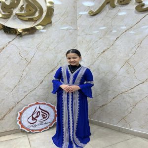 Jeune fille souriante portant une djellaba égyptienne bleu roi ornée de larges bandes de broderies argentées et dorées de style caftan.