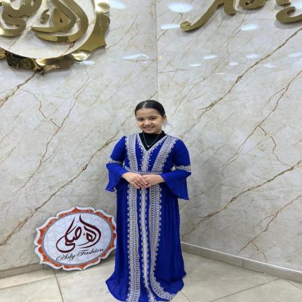 Jeune fille souriante portant une djellaba égyptienne bleu roi ornée de larges bandes de broderies argentées et dorées de style caftan.