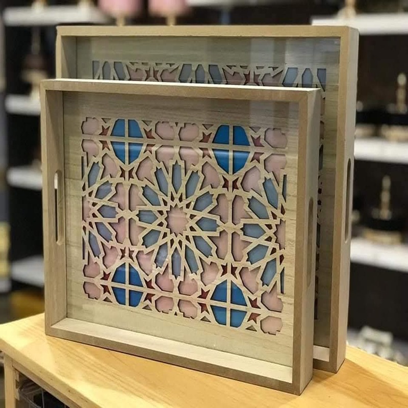 lot-2-plateaux-bois-motif-oriental.jpg Deux plateaux rectangulaires en bois clair avec fond à motifs géométriques ajourés de style oriental bleu et rose, empilés sur une table.